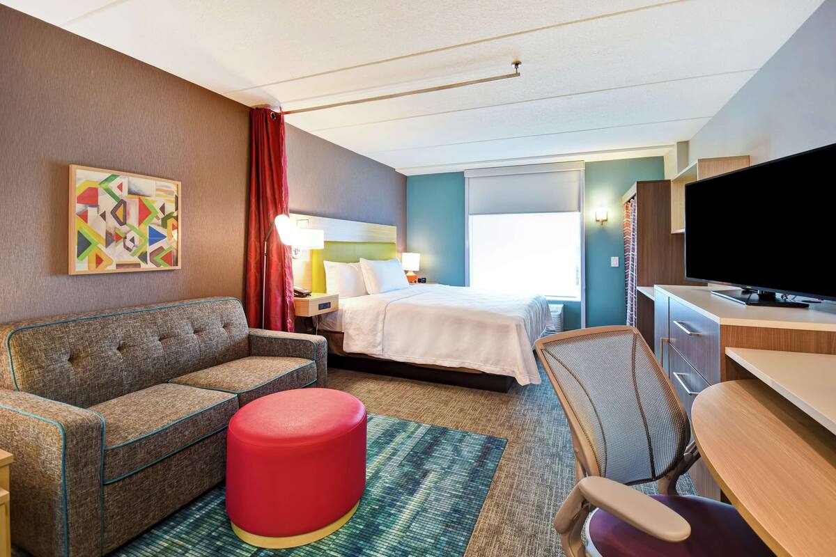 Une chambre d’hôtel avec un lit, un canapé, un bureau, une télévision et un tableau au mur.
