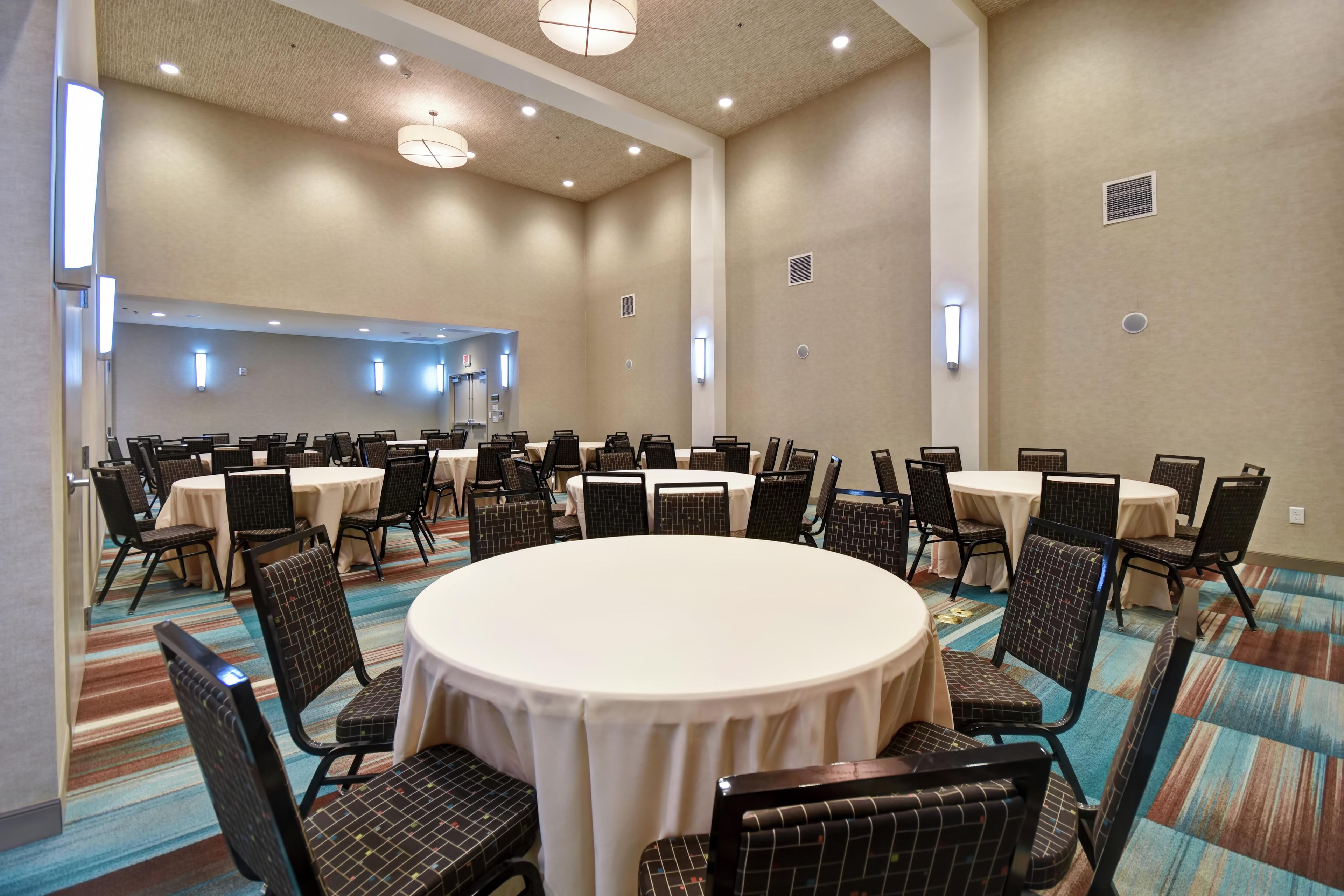 Un salón de conferencias con varias mesas y sillas, equipado con luces de techo y lámparas de pared.