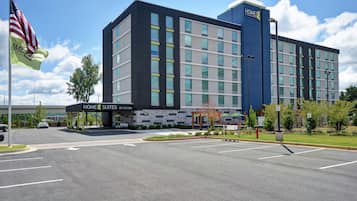 A modern hotel with a prominent 'HOME 2 SUITES BY HILTON' sign, a parking lot, and a flagpole with the American flag.