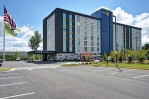 A modern hotel with a prominent 'HOME 2 SUITES BY HILTON' sign, a parking lot, and a flagpole with the American flag. - Home2 Suites by Hilton Atlanta Marietta (Marietta)