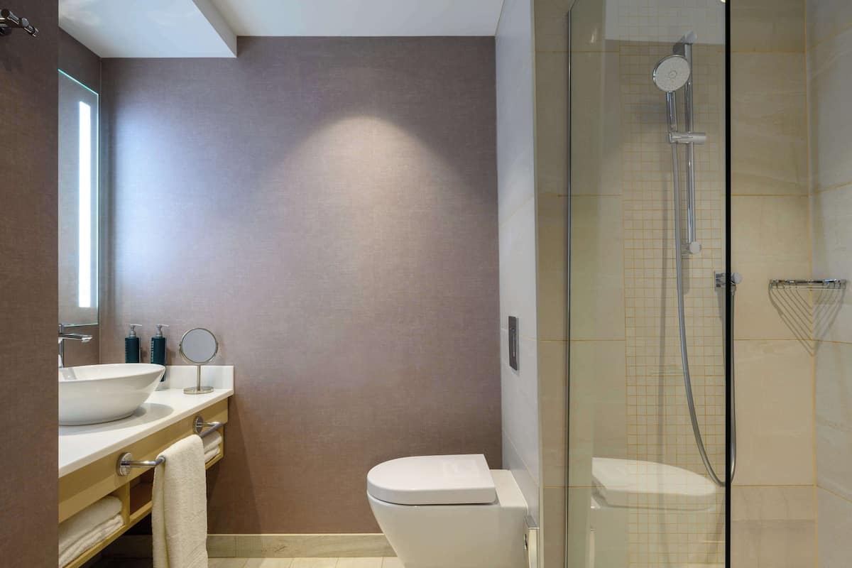 Un baño moderno con un espejo grande, un lavamanos blanco y una ducha con mampara de vidrio.