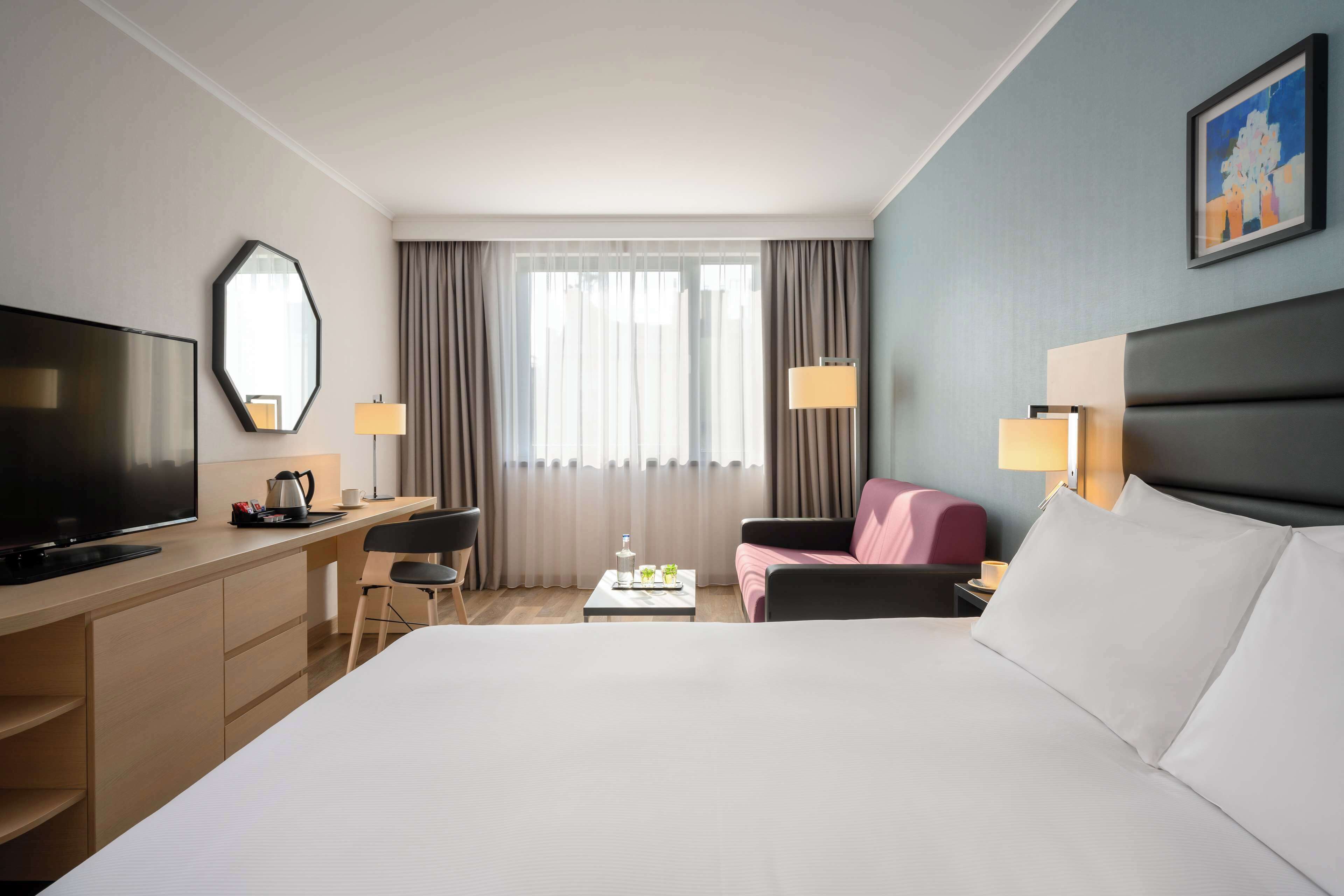 A hotel room with a large bed, a desk with a television, a chair, a coffee table, and a couch.