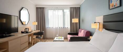A hotel room with a large bed, a desk with a television, a chair, a coffee table, and a couch.