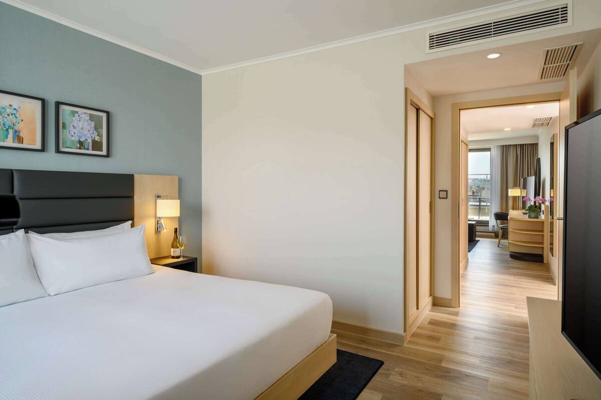 Habitación de hotel con una cama grande, un televisor de pantalla plana, una mesita de noche con lámpara y una obra de arte en la pared.