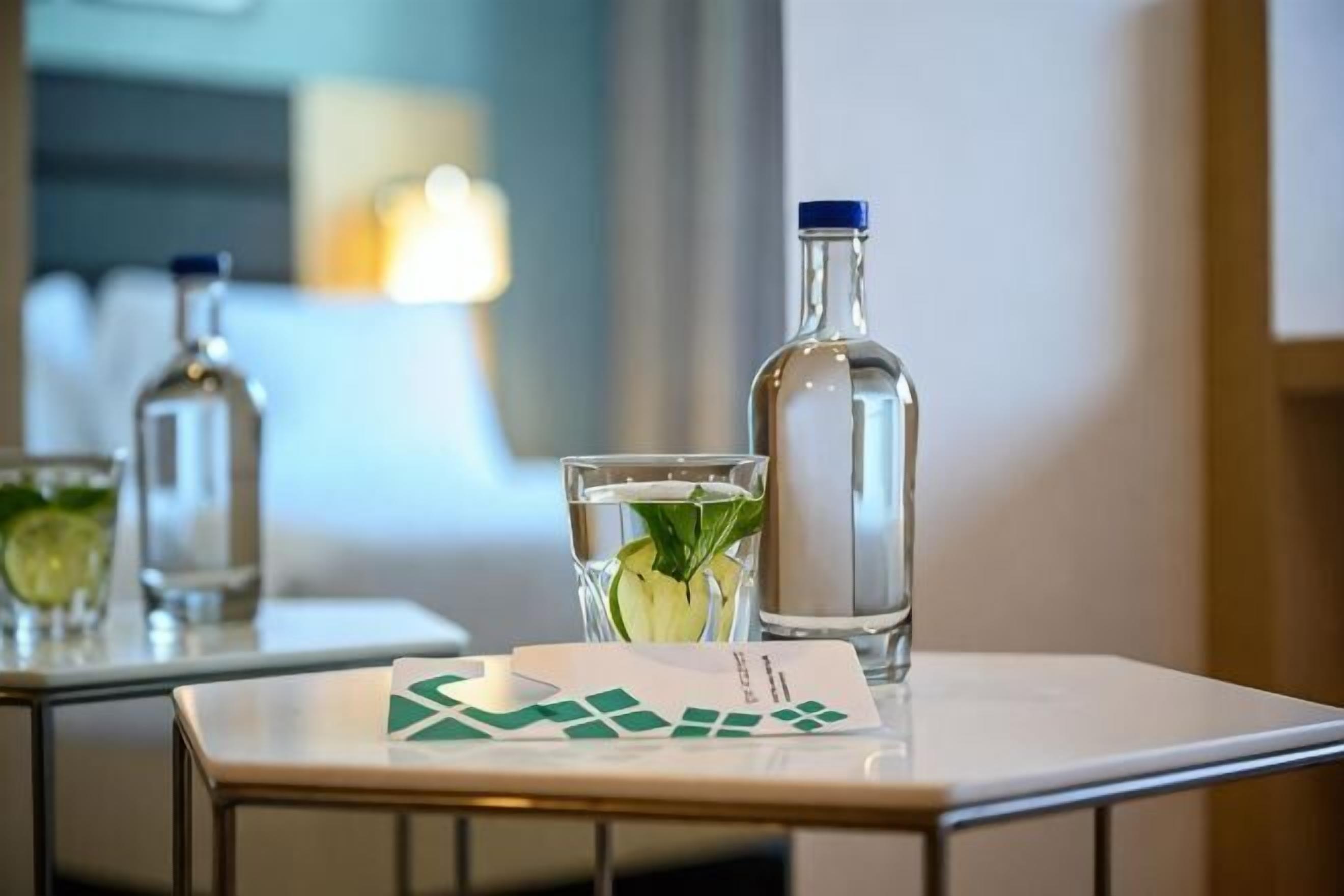 Une table avec une bouteille d’eau, un verre décoré d’une feuille de menthe et une carte posée sur une table de chambre d’hôtel.