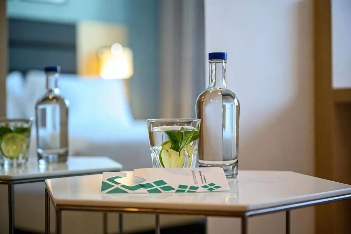 Una mesa con una botella de agua, un vaso adornado con una hoja de menta y una tarjeta sobre la mesa de la habitación de hotel.
