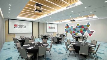 A conference room at Hilton Garden Inn with multiple tables and chairs, a projector screen, and a geometric wall decoration.