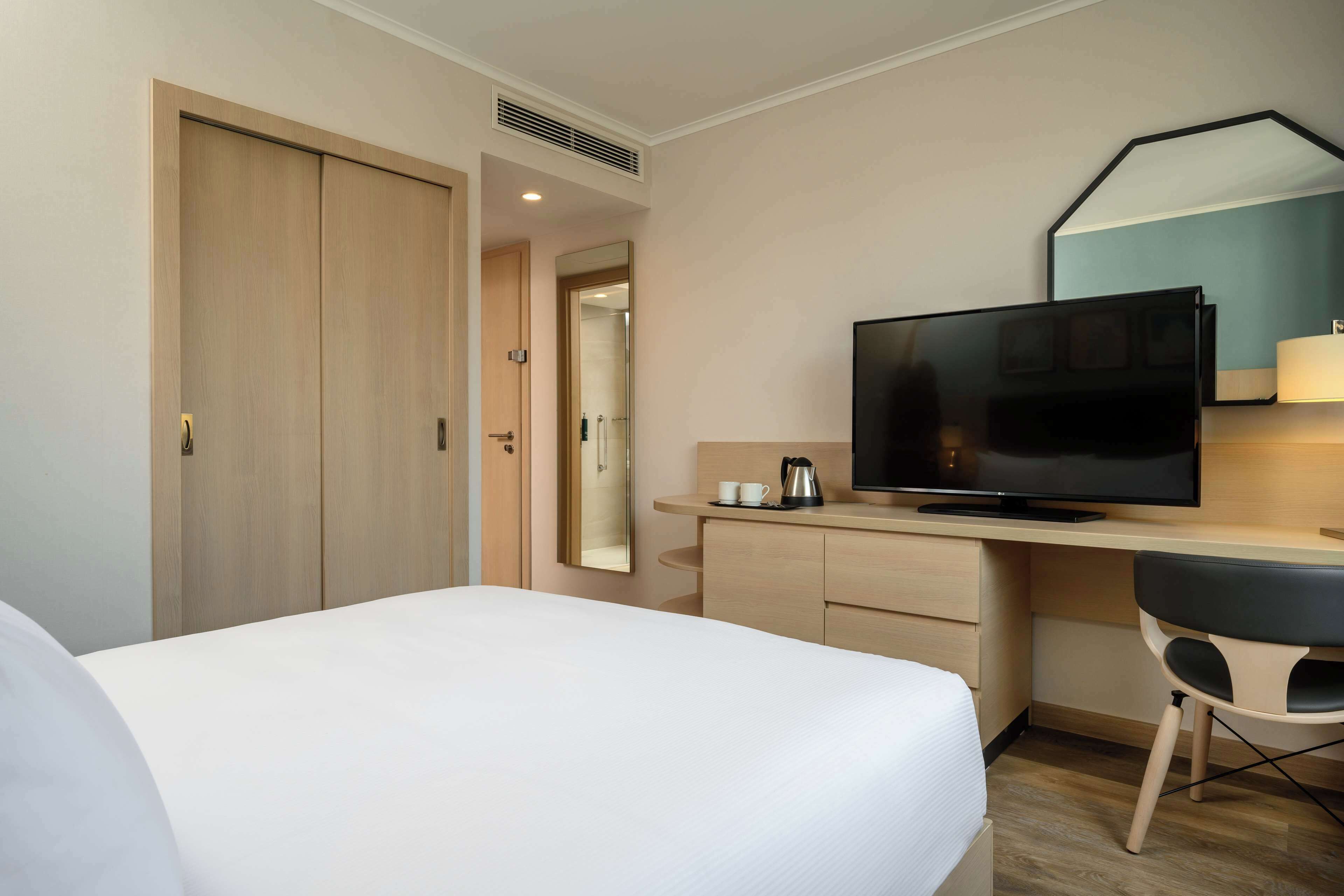 Una habitación de hotel con cama, escritorio con televisor, espejo y cafetera.