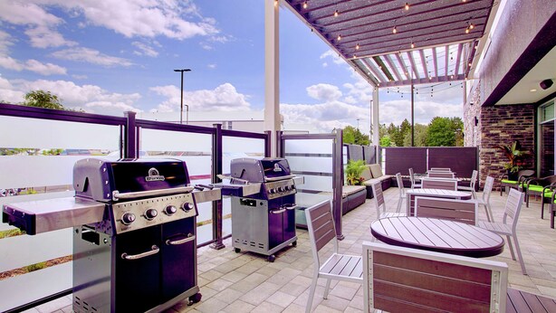 An outdoor patio with two barbecue grills, seating area, and a view of the water. - Home2 Suites by Hilton Toronto Brampton (Brampton)