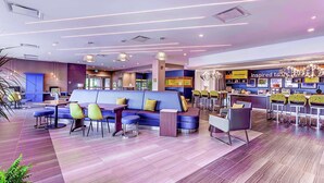 A modern hotel lobby with a blue sofa, yellow and green chairs, a bar area, and a reception desk. - Home2 Suites by Hilton Toronto Brampton (Brampton)