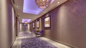 A hotel hallway with a purple carpet, framed artwork on the walls, and purple chairs. - Home2 Suites by Hilton Toronto Brampton (Brampton)