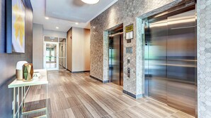 A modern hotel lobby with a polished wood floor, a reception desk, and two elevators. - Home2 Suites by Hilton Toronto Brampton (Brampton)