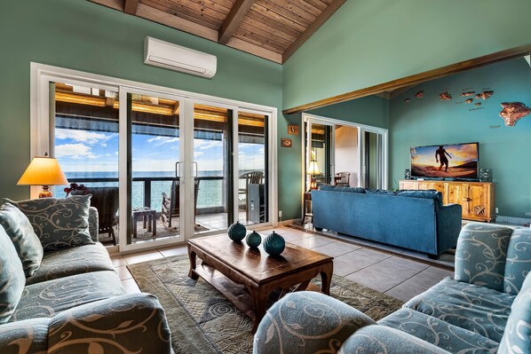 A spacious living room with a view of the ocean, a blue sofa, a wooden coffee table, and a television. - Keauhou Kona Surf & Racquet Club #5-303 (Kailua-Kona)