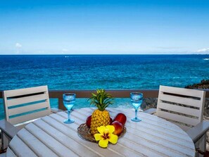 A table with a pineapple, two glasses, and a flower on a wooden deck overlooking the ocean. - Keauhou Kona Surf & Racquet Club #5-303 (Kailua-Kona)