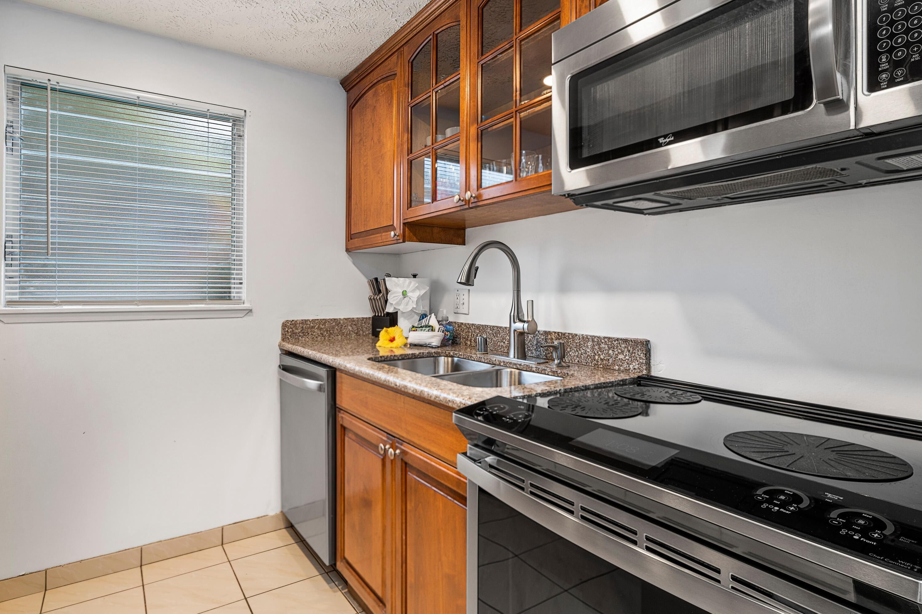 A kitchen with wooden cabinets, a stainless steel microwave, a stove, and a sink.