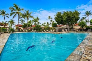 Una piscina con agua azul cristalina, rodeada de palmeras y sillas de descanso.