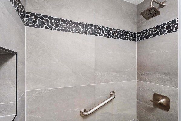 Zona de ducha con baranda, cabezal de ducha y pared de azulejos con diseño de piedritas.