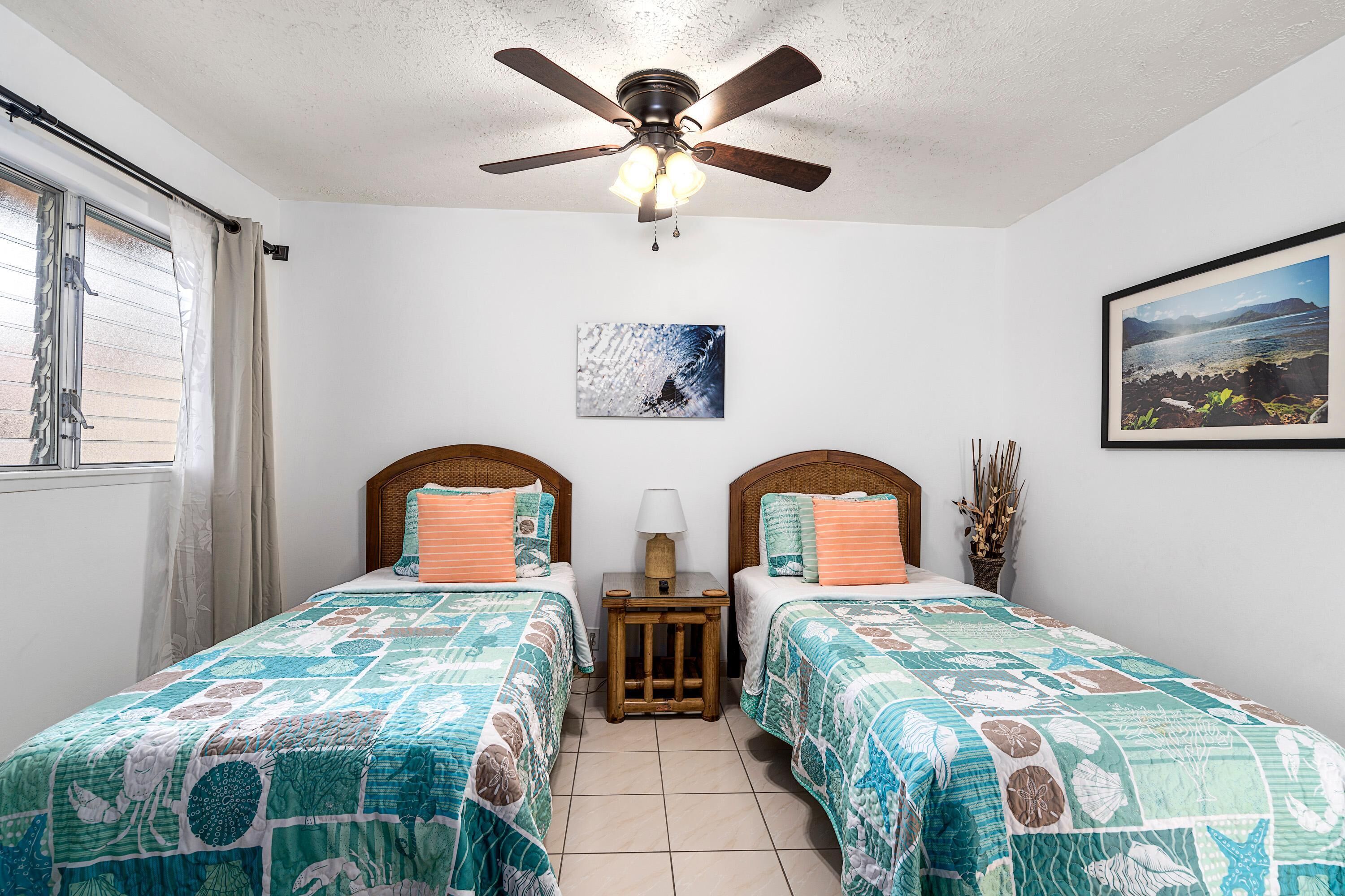 A bedroom with two beds, a ceiling fan, and a window with curtains.