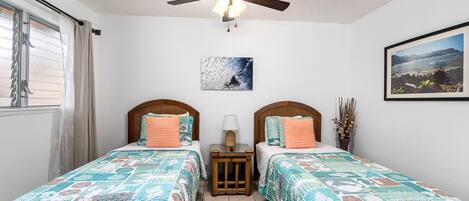 A bedroom with two beds, a ceiling fan, and a window with curtains.