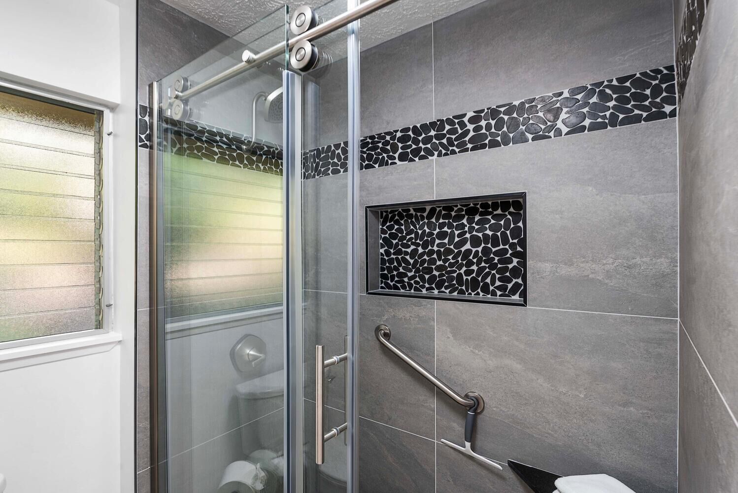 Een moderne badkamer met een glazen douchecabine, een handgreep en een decoratieve stenen tegelaccent.