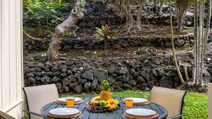 Une table ronde dressée pour quatre personnes, avec des assiettes, des couverts et un centre de table composé de fruits.