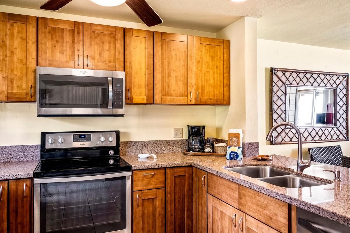 Una cocina con armarios de madera, un microondas de acero inoxidable, una estufa y un lavamanos.