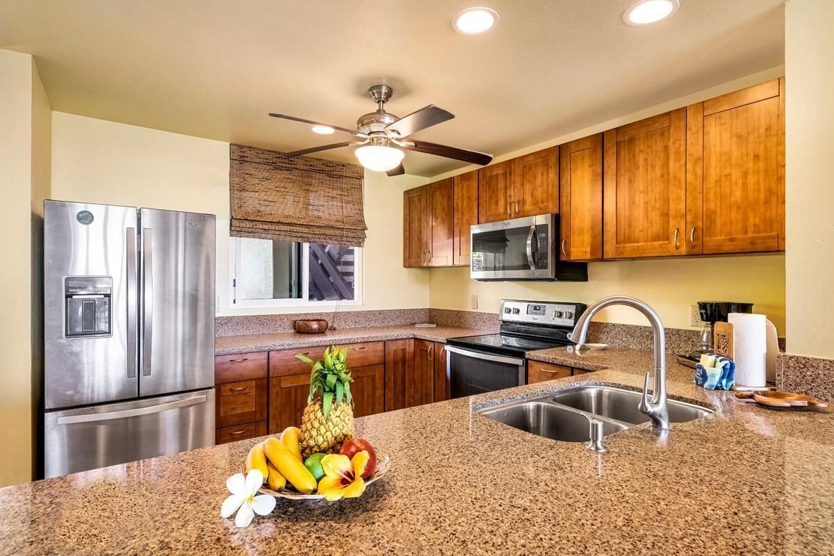 Cocina con encimeras de granito, electrodomésticos de acero inoxidable, armarios de madera y ventilador de techo.