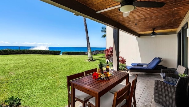 Eine überdachte Terrasse mit Holztisch und -stühlen, eine Lounge-Ecke mit blauen Kissen und Meerblick.