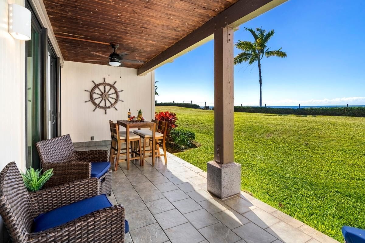 Un patio abrité, aménagé avec des meubles en osier, une table et des chaises.