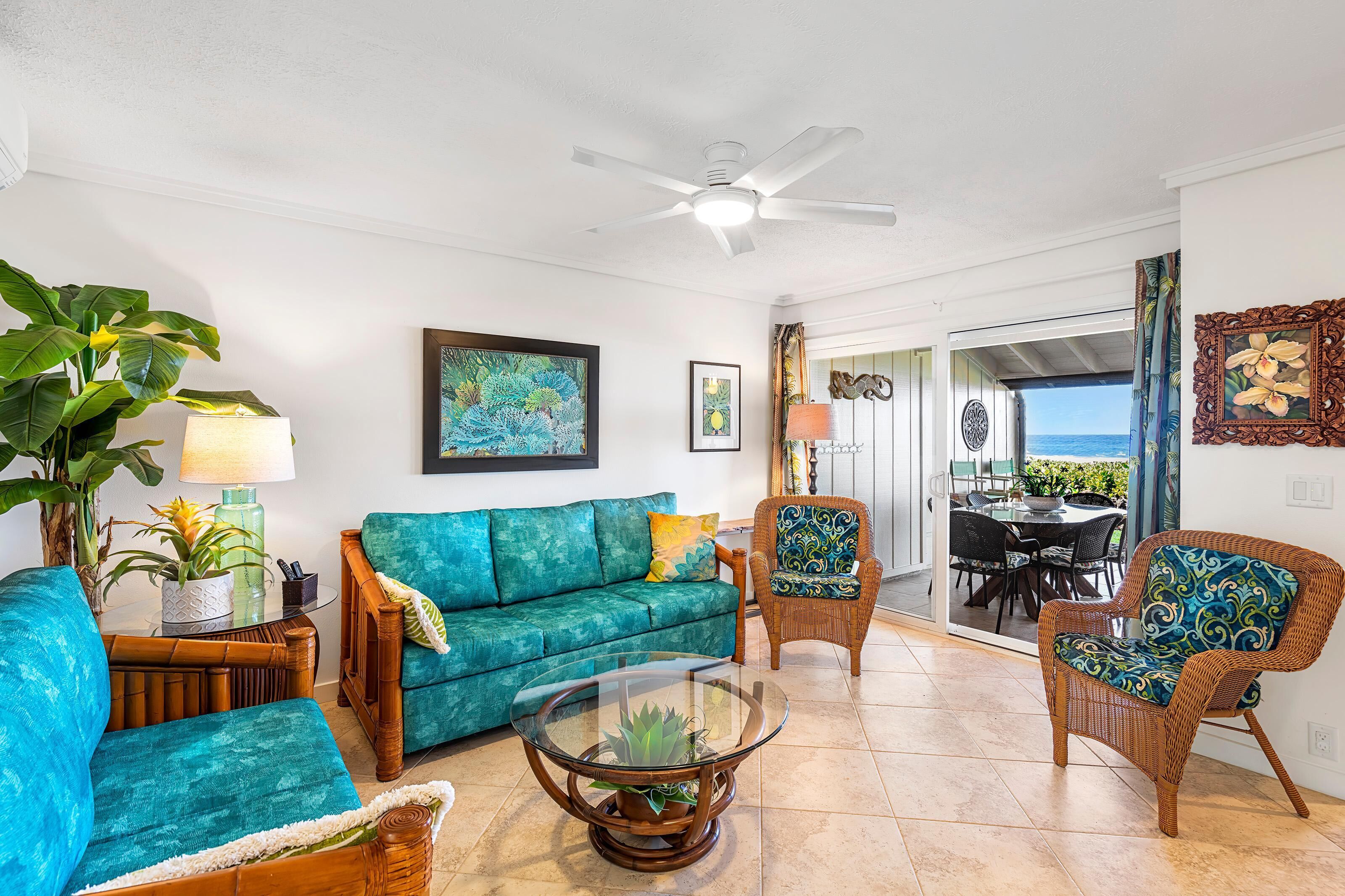 A living room with a teal sofa, wicker chairs, a glass coffee table, and a ceiling fan.