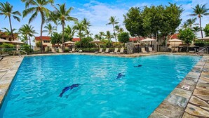 A swimming pool with clear blue water, surrounded by palm trees and lounge chairs.