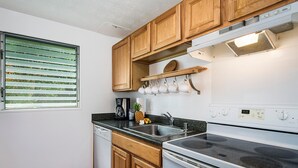 Eine Küche mit Holzausbau, einer Edelstahl-Spüle, einem Einbauofen und einem Fenster mit Jalousien.