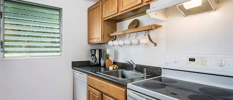 Una cocina con armarios de madera, un lavamanos de acero inoxidable, horno integrado y una ventana con persianas.