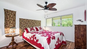 Ein Schlafzimmer mit Bett, Deckenventilator, Fenster mit Jalousien, Nachttisch und einem Holzschrank.