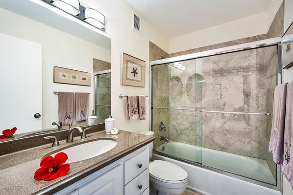 A bathroom with a glass-enclosed shower, a white toilet, and a sink with a marble countertop.
