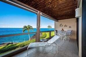 A balcony with a view of the ocean, a table with chairs, and a lounge chair.