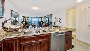 Una cocina con encimeras de granito, gabinetes de madera, lavavajillas y vista al océano.