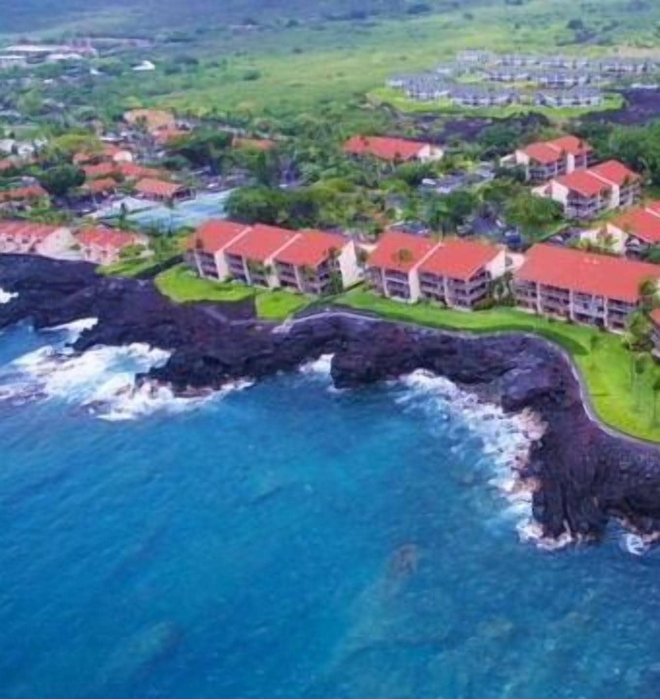 A coastal resort with multiple buildings featuring red roofs, situated on a rocky shoreline with clear blue waters.