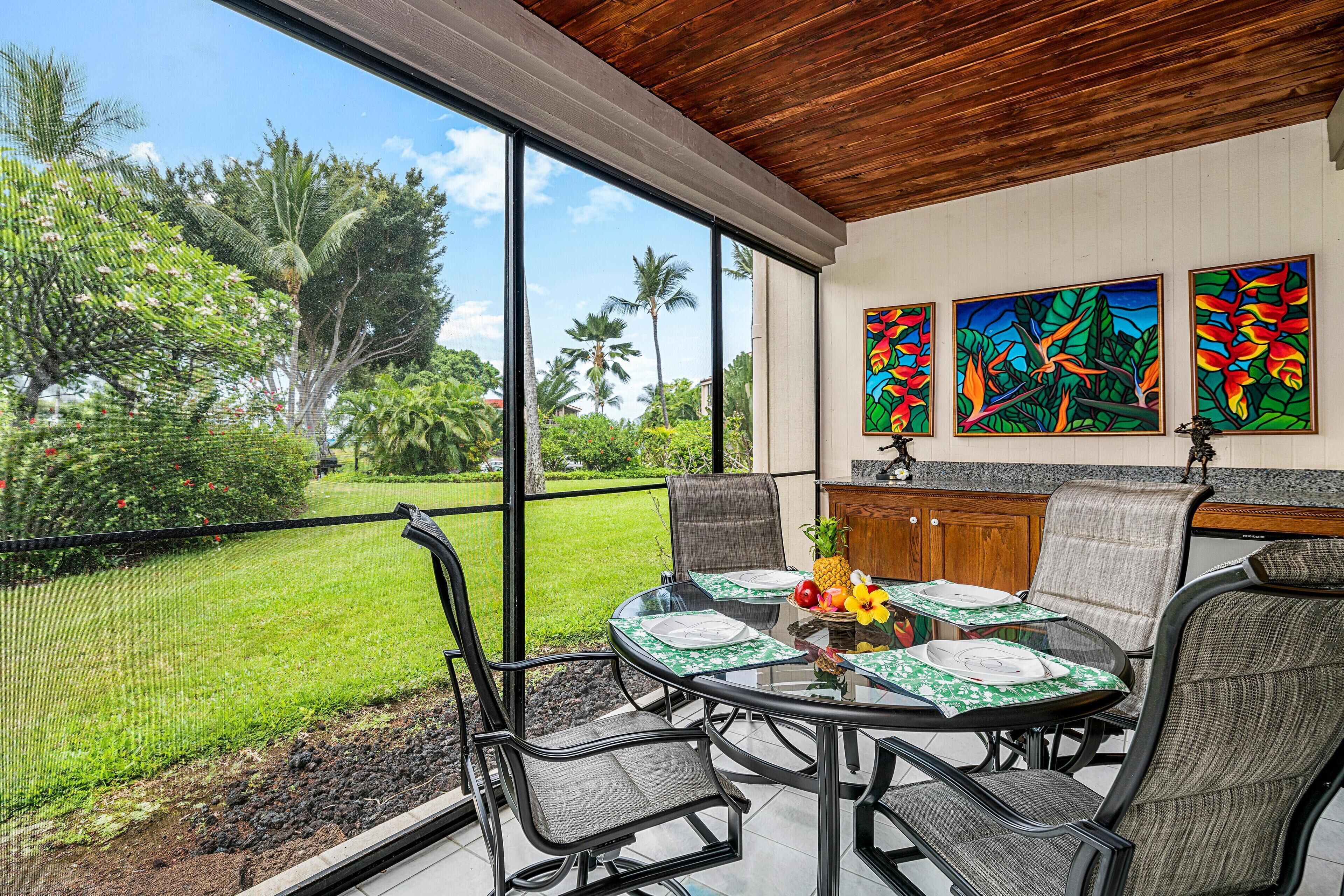Un'area pranzo con vista su un giardino rigoglioso, un soffitto in legno e tre quadri colorati appesi alla parete.
