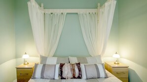 Uma cama com dossel, duas mesas de cabeceira com luminárias e um criado-mudo com gaveta.