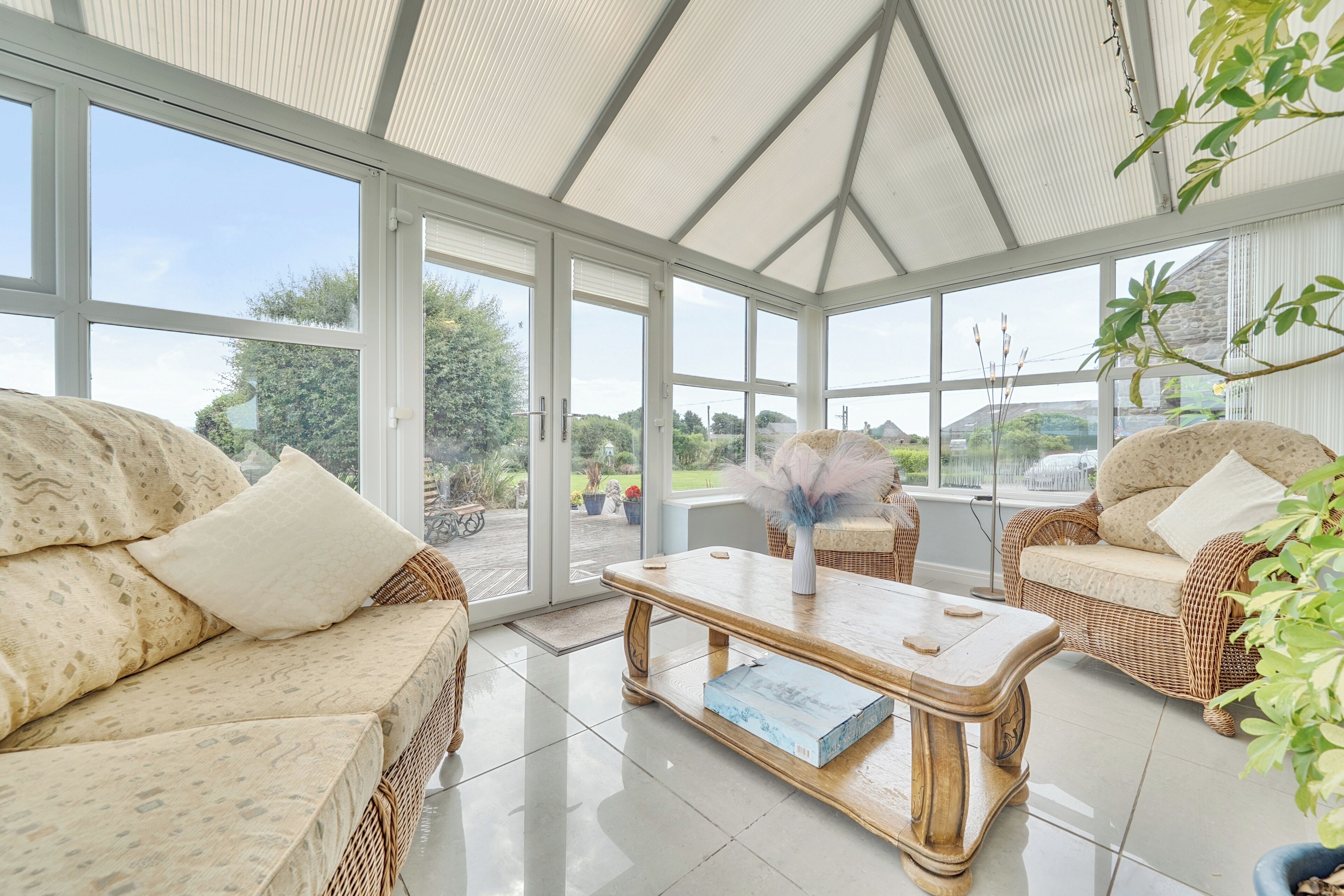 A conservatory with wicker furniture, a glass table, and a view of the outdoors.