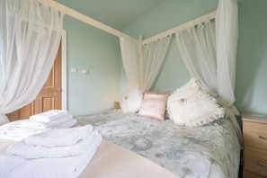 A bedroom with a four-poster bed, white curtains, and a bedside table with a lamp.