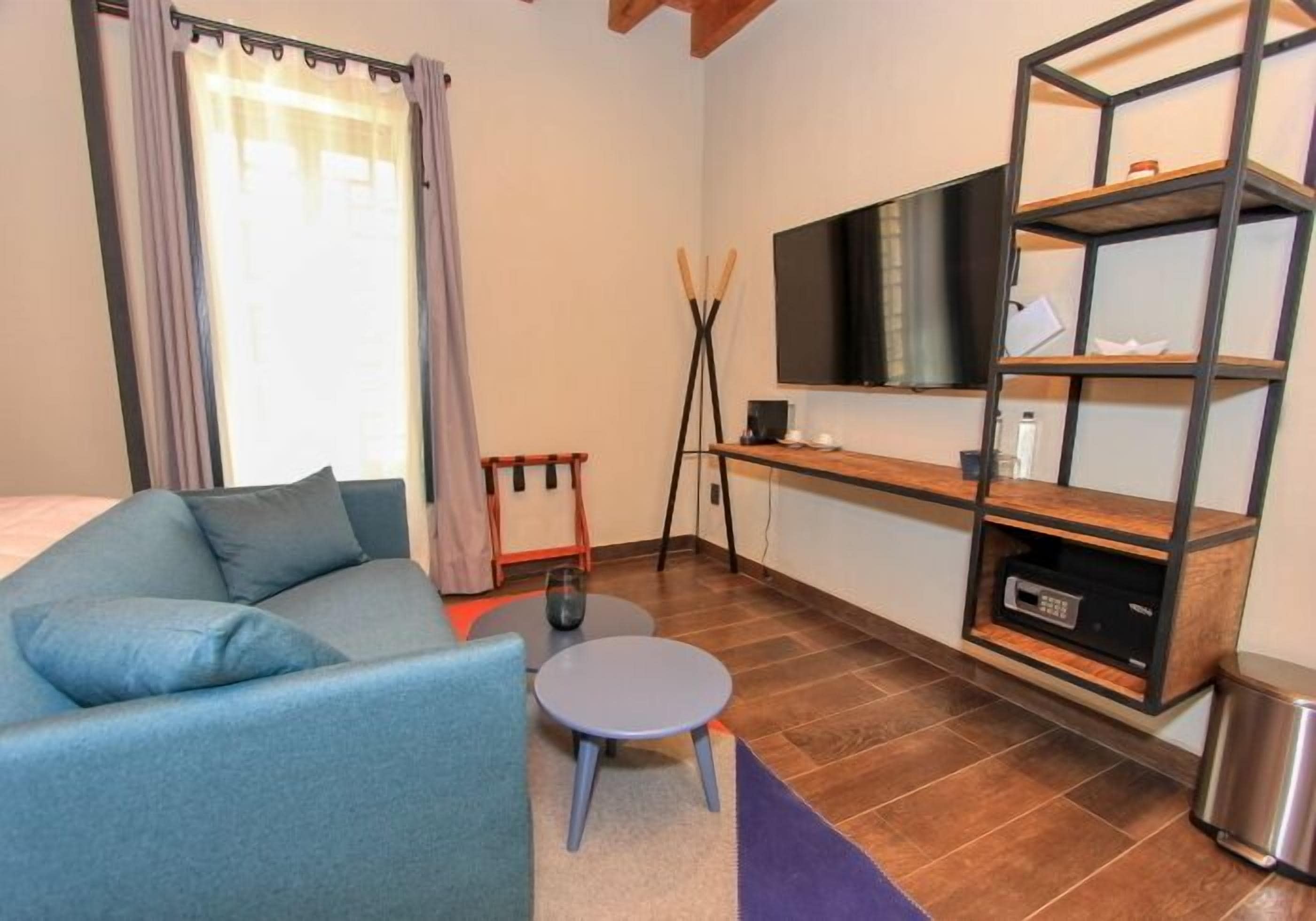 A modern room with a sofa, a small table, a TV mounted on a wall, and a wooden shelf unit.