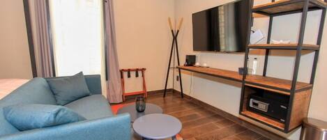 A modern room with a sofa, a small table, a TV mounted on a wall, and a wooden shelf unit.