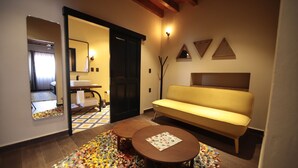 Un interior moderno con un sofá, dos mesitas, un espejo y una puerta que da a un baño.