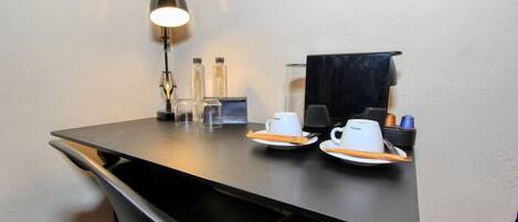 A small, modern room with a desk, two white cups, a black lamp, and a black chair.