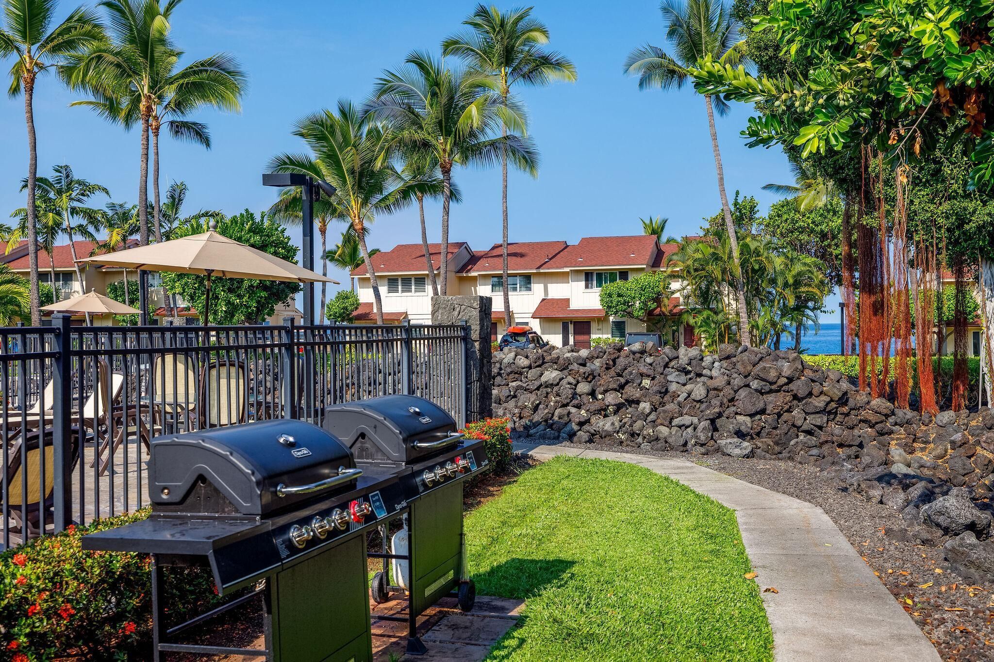 A barbecue area with grills, a stone wall, and a pathway leading to a building with a red roof.