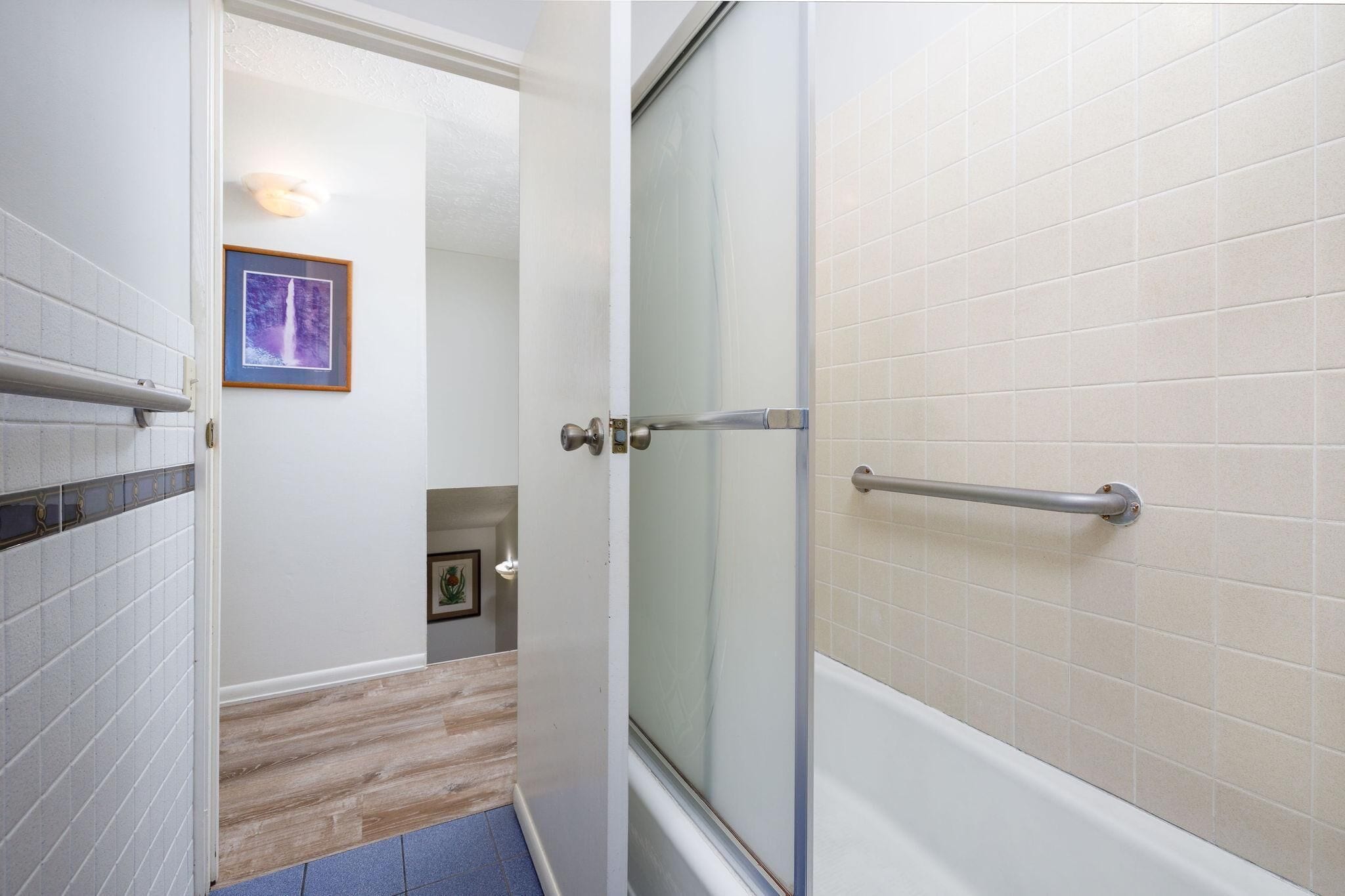 A bathroom with a glass shower door, a handrail, and tiled walls.