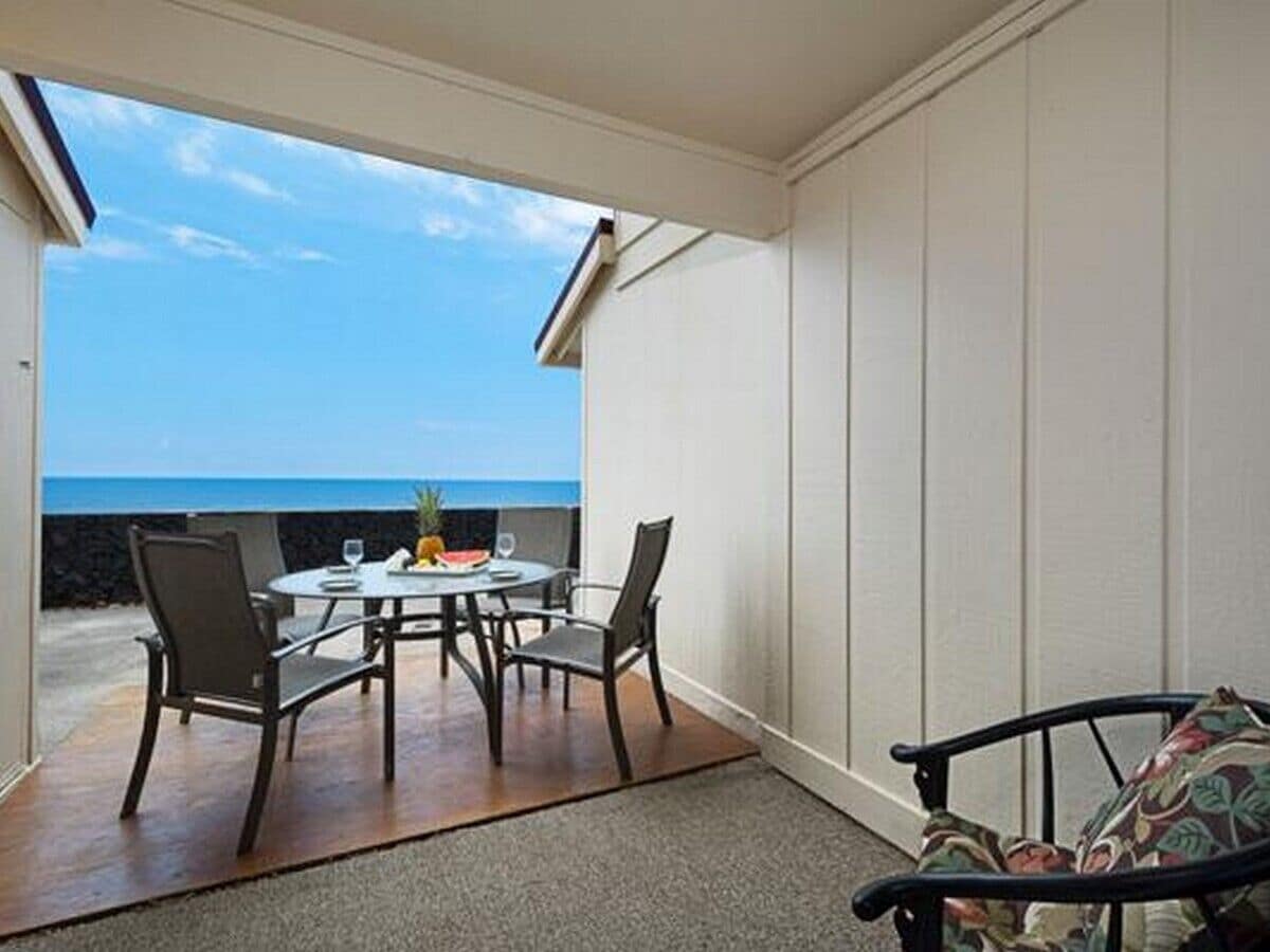 Alpendre coberto com mesa e cadeiras, com vista para o oceano.