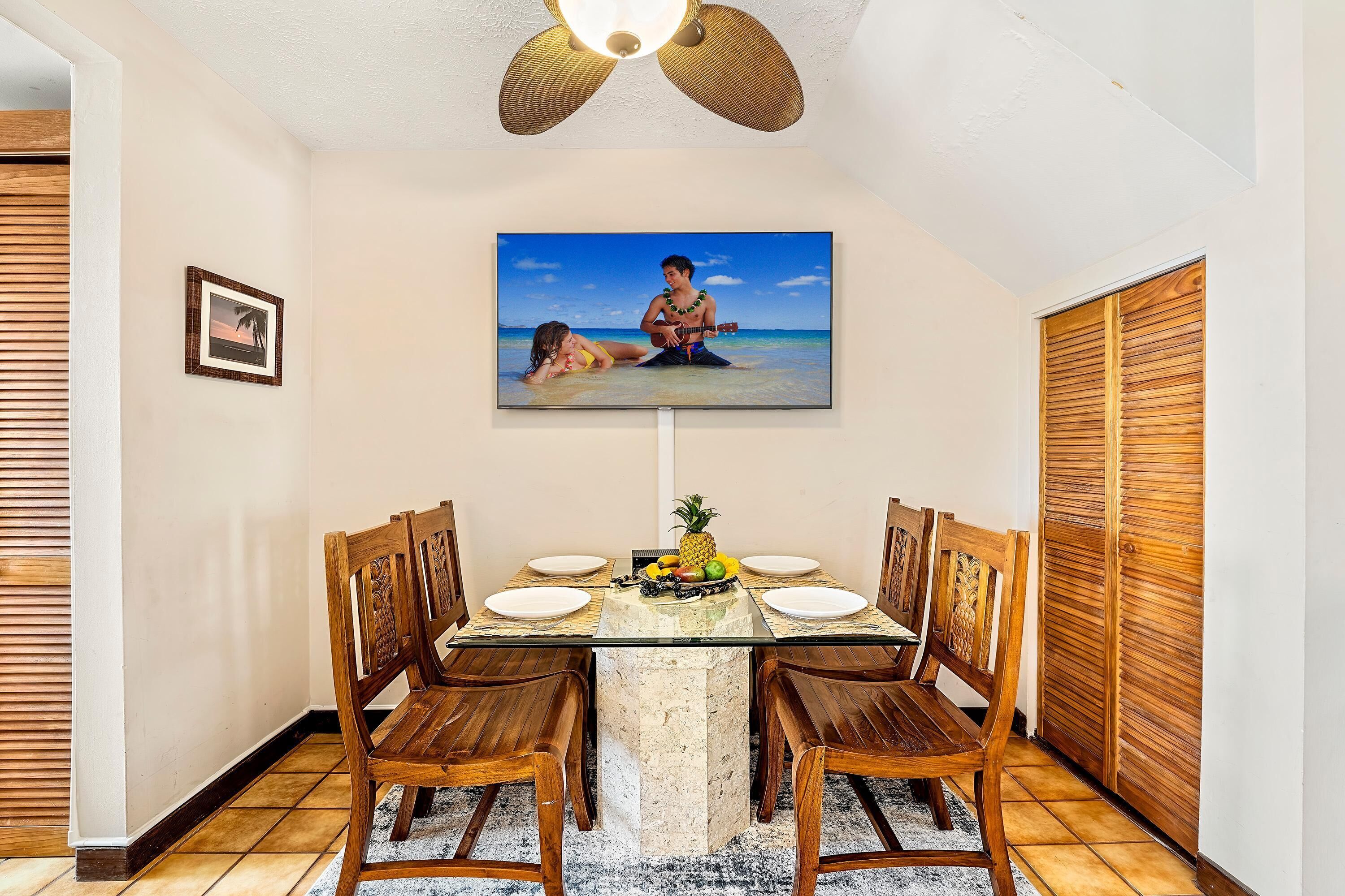 Un comedor con una mesa de vidrio, sillas de madera y un cuadro con temática tropical.